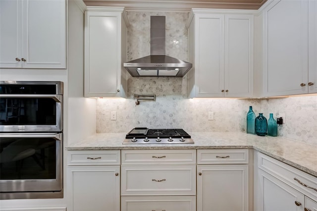 kitchen with wall chimney exhaust hood, stainless steel appliances, white cabinetry, and tasteful backsplash