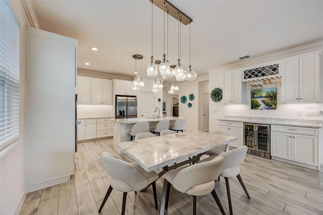 dining room with beverage cooler, ornamental molding, a dry bar, wood finish floors, and recessed lighting