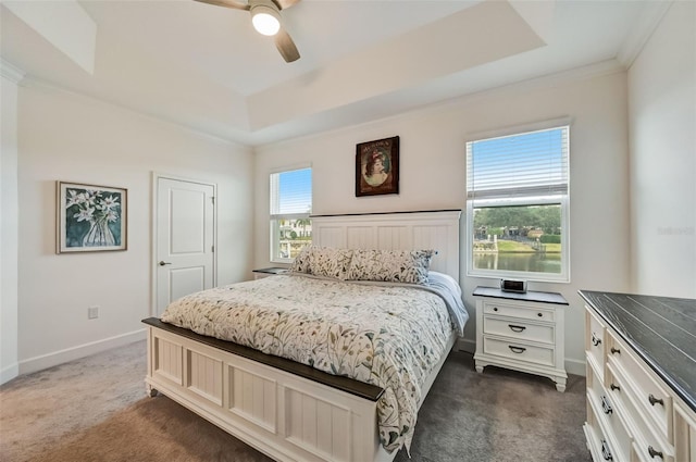 bedroom with dark colored carpet, a tray ceiling, baseboards, ornamental molding, and a ceiling fan