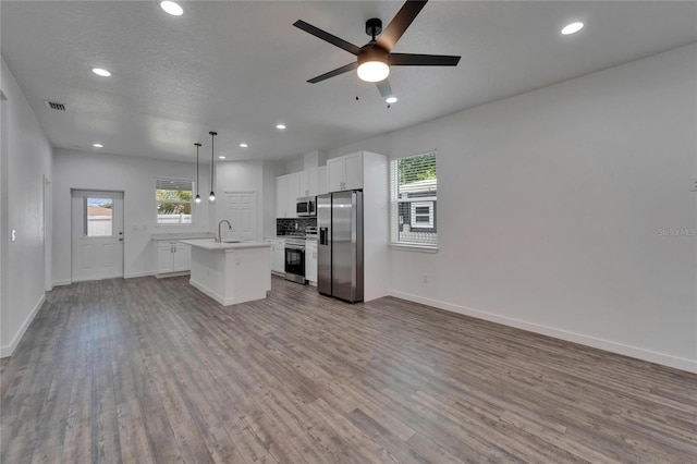 6097 Vermont Ave, New Port Richey, FL 34653 - kitchen with stainless steel appliances, a ceiling fan, a center island with sink, light countertops, and wood finished floors