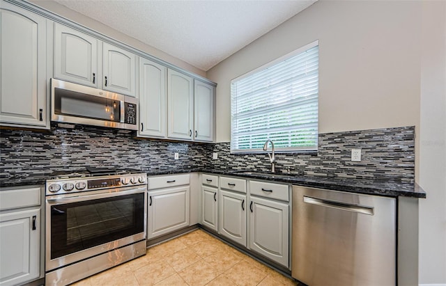 1712 Crossvine Ct, Trinity, FL 34655 - kitchen with appliances with stainless steel finishes, decorative backsplash, light tile patterned floors, dark stone counters, and a textured ceiling