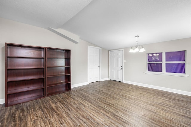empty room featuring a chandelier, wood finished floors, vaulted ceiling, and baseboards