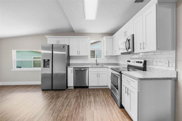 kitchen featuring stainless steel appliances, a sink, wood finished floors, white cabinetry, and vaulted ceiling