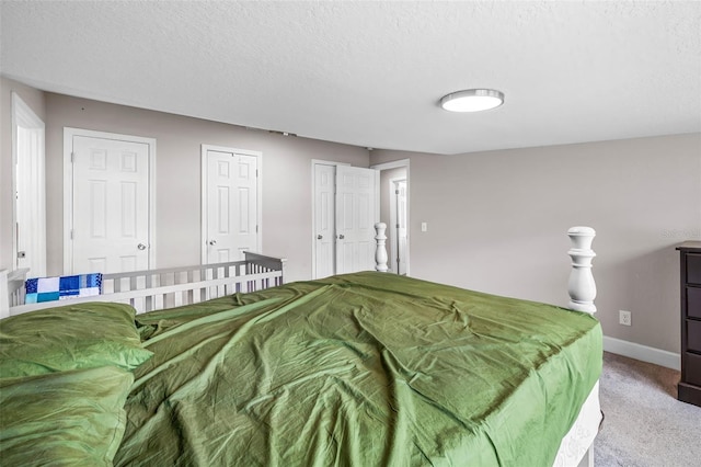 bedroom with carpet floors, a textured ceiling, baseboards, and two closets