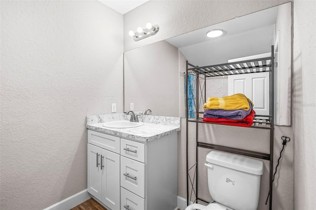 bathroom with vanity, a textured wall, toilet, and wood finished floors