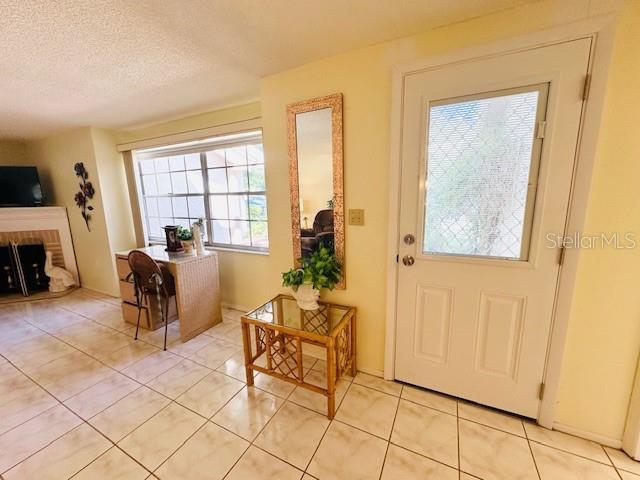 doorway to outside with light tile patterned floors, a textured ceiling, and a brick fireplace