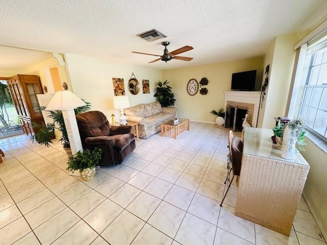 living room with ceiling fan, a brick fireplace, a textured ceiling, and light tile patterned floors