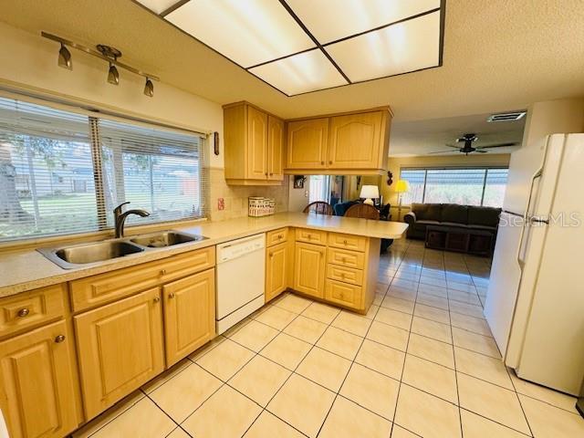 kitchen featuring white appliances, a sink, a peninsula, light tile patterned floors, and light countertops