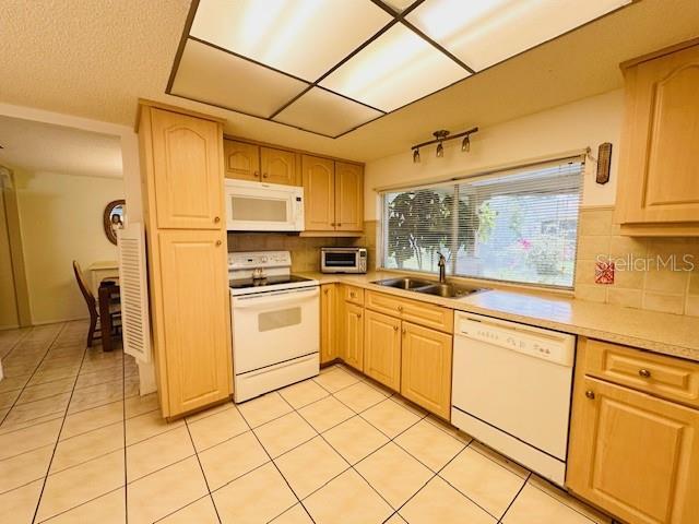 kitchen with white appliances, a sink, tasteful backsplash, light countertops, and light tile patterned flooring