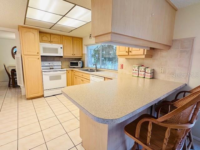 kitchen with white appliances, light brown cabinets, a sink, light countertops, and a kitchen bar