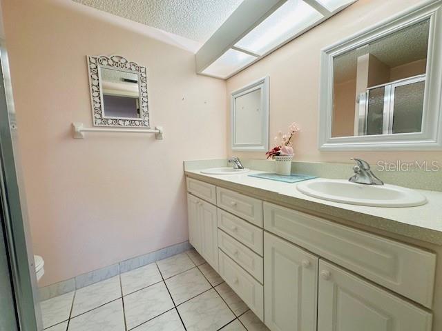bathroom featuring double vanity, a textured ceiling, a stall shower, tile patterned floors, and toilet