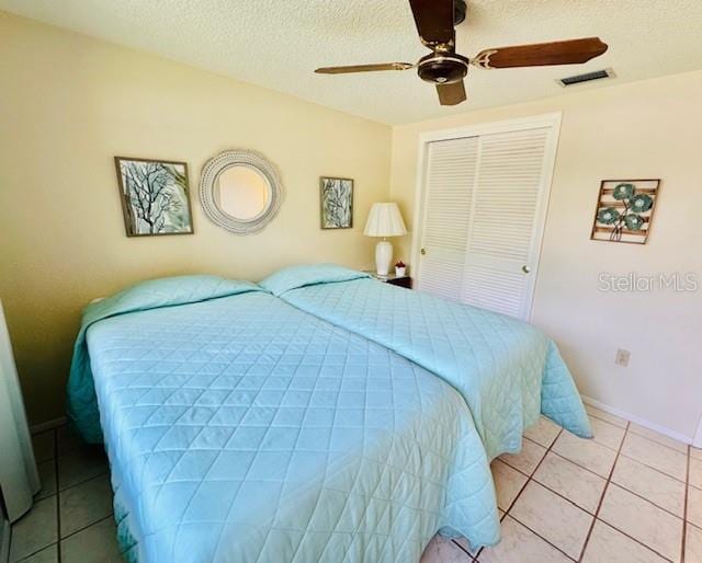 bedroom with a closet, light tile patterned floors, a ceiling fan, a textured ceiling, and baseboards