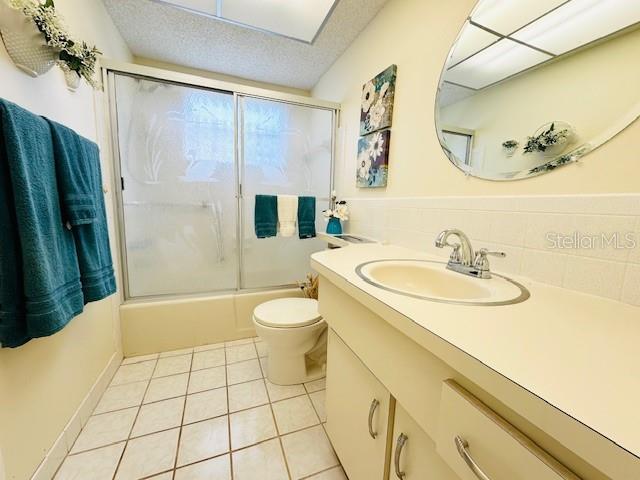 full bathroom featuring tile patterned floors, vanity, toilet, combined bath / shower with glass door, and a textured ceiling