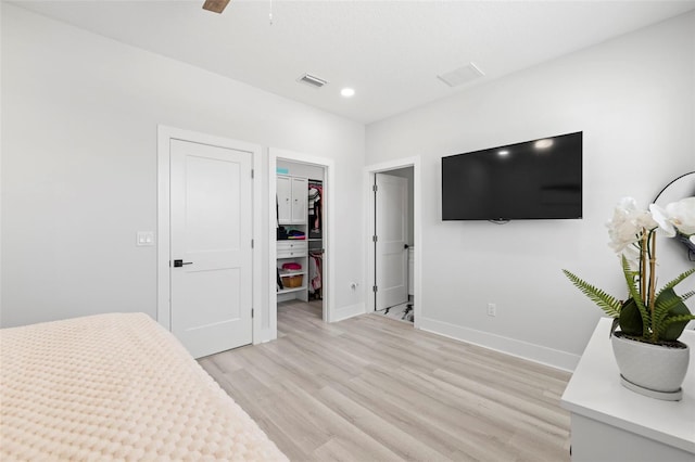 bedroom with a walk in closet, light wood finished floors, baseboards, a closet, and recessed lighting