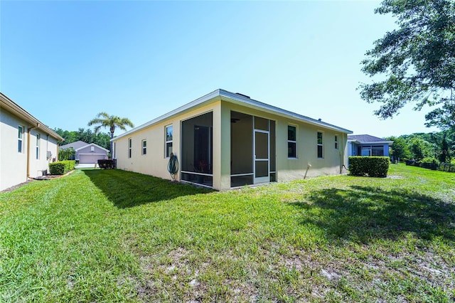 back of property with a yard, a sunroom, and stucco siding