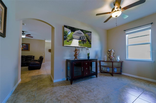 tiled living area with arched walkways, a ceiling fan, and baseboards