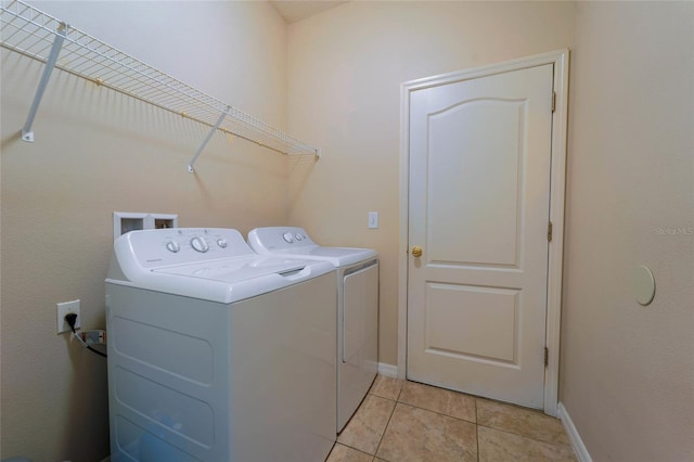 clothes washing area featuring washer and clothes dryer, light tile patterned floors, and baseboards