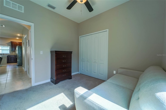 bedroom with freestanding refrigerator, light carpet, arched walkways, a closet, and baseboards