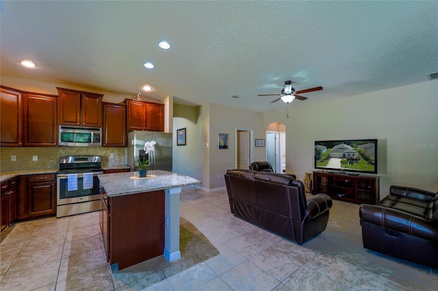 kitchen featuring stainless steel appliances, open floor plan, arched walkways, a kitchen island, and light stone counters
