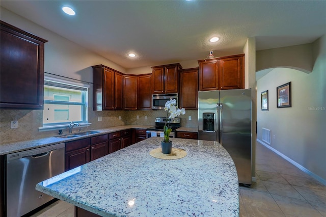 kitchen with stainless steel appliances, a sink, arched walkways, tasteful backsplash, and recessed lighting