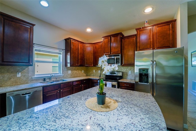 kitchen featuring stainless steel appliances, a sink, light stone countertops, backsplash, and recessed lighting