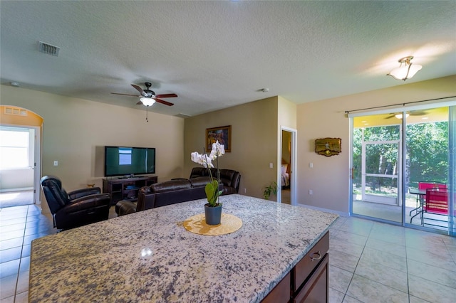 kitchen with plenty of natural light, a ceiling fan, a textured ceiling, light stone countertops, and light tile patterned floors