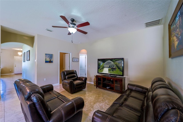 living area featuring arched walkways, tile patterned floors, a ceiling fan, and a textured ceiling