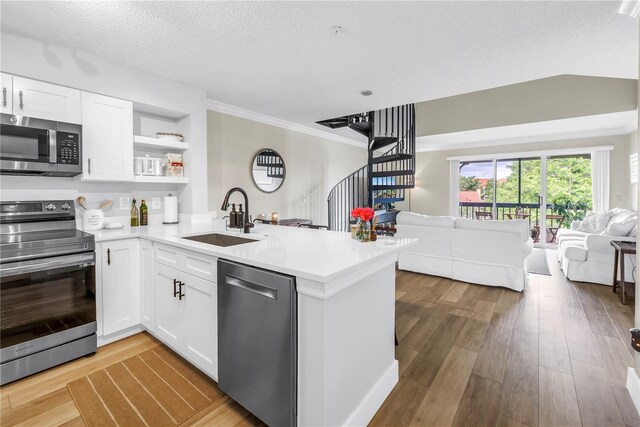 kitchen with stainless steel appliances, a sink, open floor plan, a peninsula, and white cabinetry