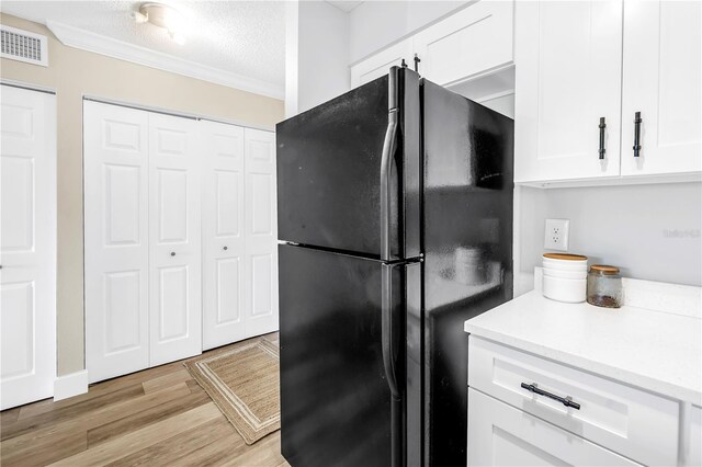 kitchen featuring freestanding refrigerator, crown molding, white cabinets, a textured ceiling, and light wood-style flooring