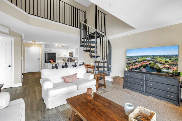 living room featuring stairway, wood finished floors, crown molding, and baseboards