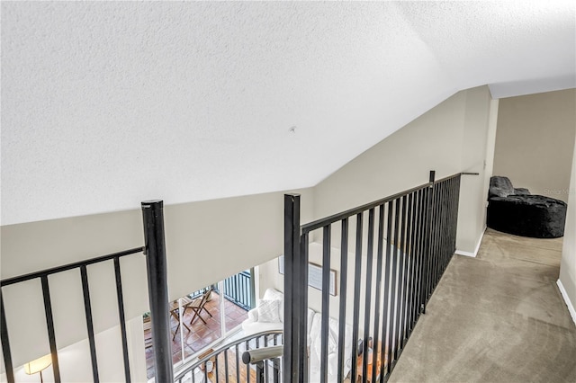 corridor with a textured ceiling, an upstairs landing, carpet flooring, and lofted ceiling