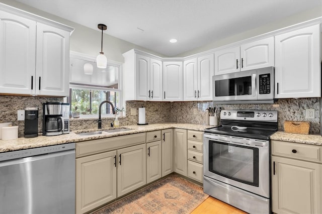 kitchen featuring appliances with stainless steel finishes, a sink, pendant lighting, backsplash, and light stone countertops