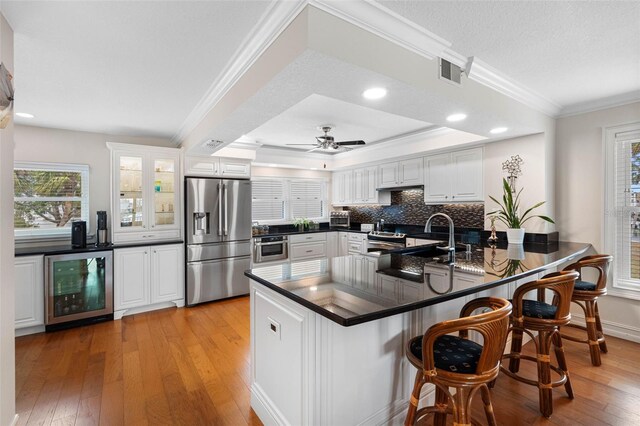 12360 Capri Cir N Unit 106, Treasure Island, FL 33706 - kitchen featuring stainless steel appliances, beverage cooler, dark countertops, light wood-type flooring, and ornamental molding