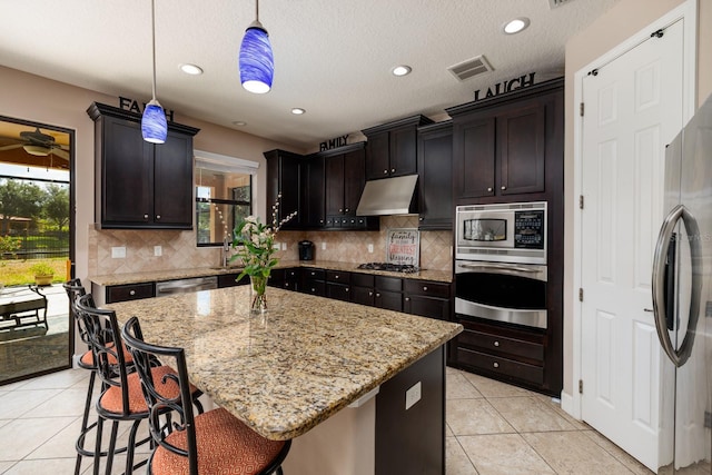 4611 Grand Preserve Pl, Palm Harbor, FL 34684 - kitchen with appliances with stainless steel finishes, under cabinet range hood, light tile patterned floors, light stone counters, and backsplash