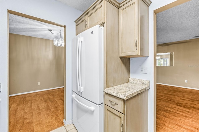 kitchen with freestanding refrigerator, a textured ceiling, light wood finished floors, baseboards, and light brown cabinets