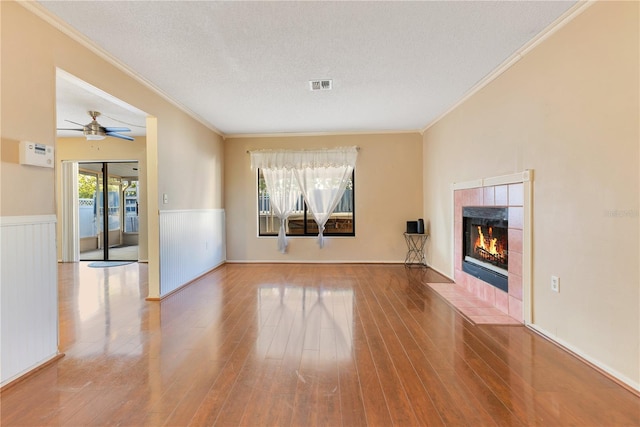 728 Waterbridge Dr, Winter Haven, FL 33880 - unfurnished living room with crown molding, a wainscoted wall, a tile fireplace, wood finished floors, and a textured ceiling