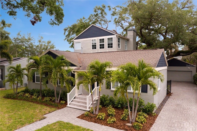 view of front of home featuring a chimney, a front lawn, an outbuilding, a detached garage, and roof with shingles