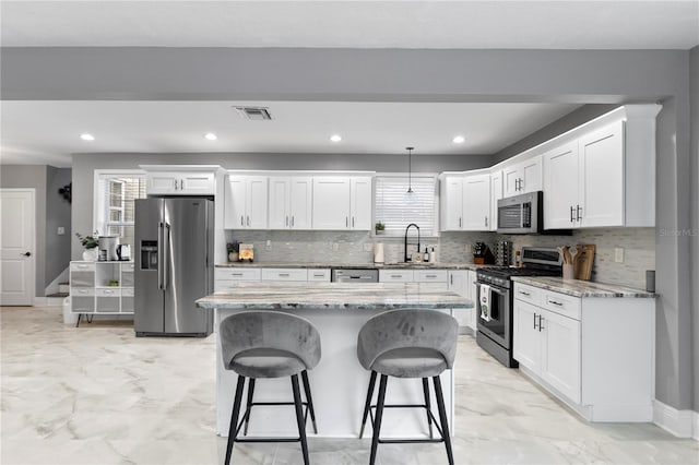 kitchen with appliances with stainless steel finishes, a breakfast bar, white cabinetry, a kitchen island, and decorative backsplash