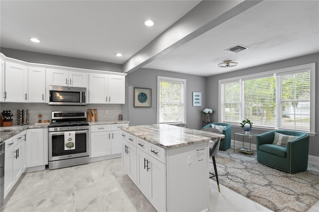 kitchen with appliances with stainless steel finishes, light marble finish floors, tasteful backsplash, a center island, and light stone counters