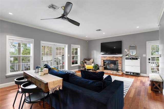 living area with a fireplace, crown molding, ceiling fan, baseboards, and wood finished floors