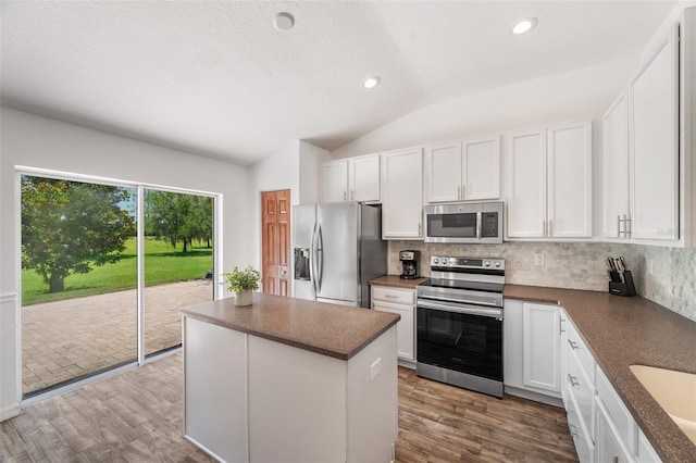 7103 Bridgeview Dr, Wesley Chapel, FL 33545 - kitchen featuring stainless steel appliances, dark countertops, decorative backsplash, vaulted ceiling, and a kitchen island