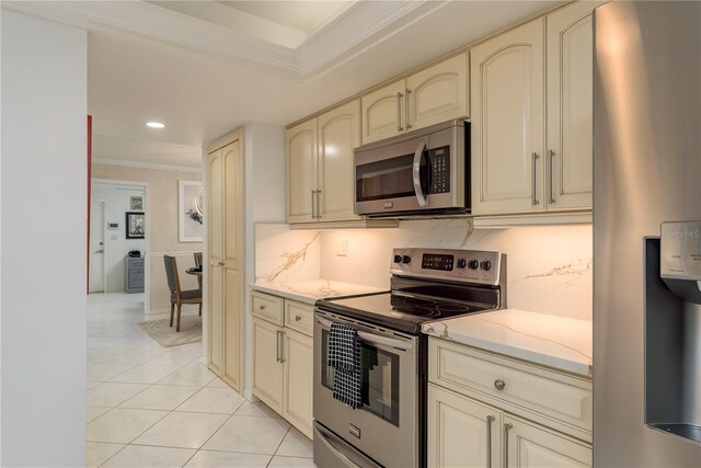 3071 Bolt Dr, Palm Harbor, FL 34685 - kitchen with cream cabinetry, appliances with stainless steel finishes, ornamental molding, light tile patterned flooring, and decorative backsplash