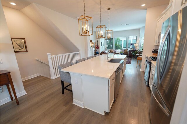 kitchen featuring appliances with stainless steel finishes, a sink, a breakfast bar area, white cabinetry, and a center island with sink