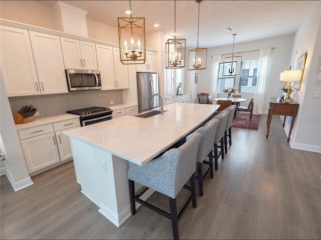 kitchen featuring stainless steel appliances, a kitchen island with sink, tasteful backsplash, a chandelier, and white cabinets