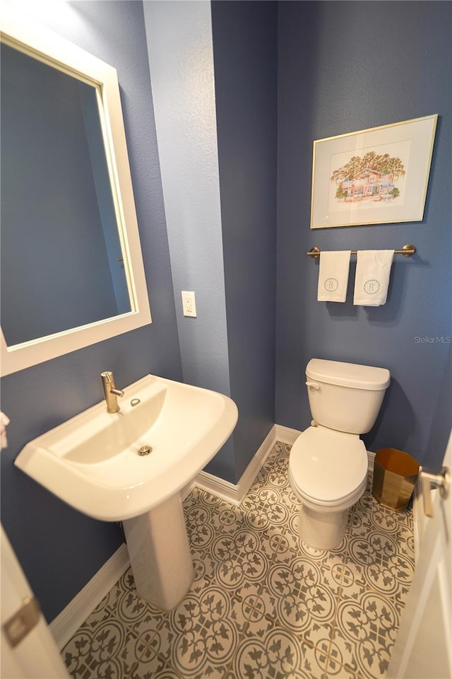 half bathroom featuring baseboards, toilet, tile patterned flooring, and a sink