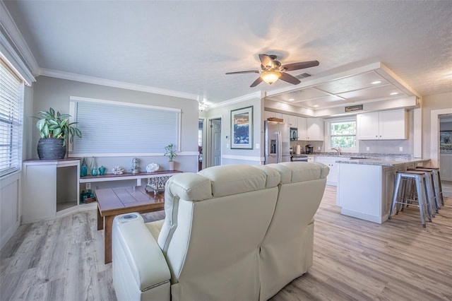 living area with light wood-type flooring, crown molding, a ceiling fan, and a raised ceiling