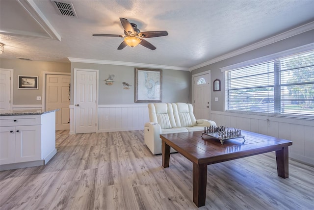 living area featuring a ceiling fan, light wood-style flooring, a wainscoted wall, and a textured ceiling