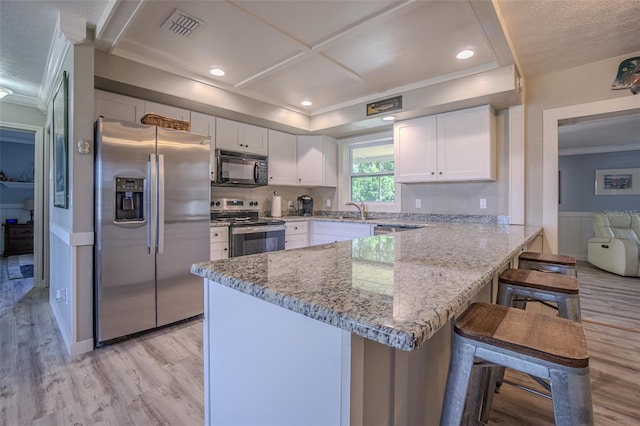 kitchen featuring stainless steel appliances, ornamental molding, a peninsula, light wood-style floors, and white cabinetry