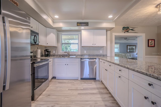 kitchen featuring appliances with stainless steel finishes, white cabinets, light wood-style flooring, light stone countertops, and ceiling fan