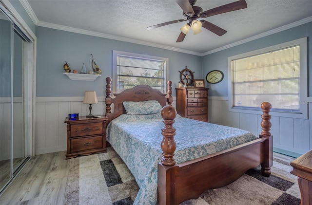 bedroom featuring wood finished floors, a wainscoted wall, a textured ceiling, crown molding, and a closet